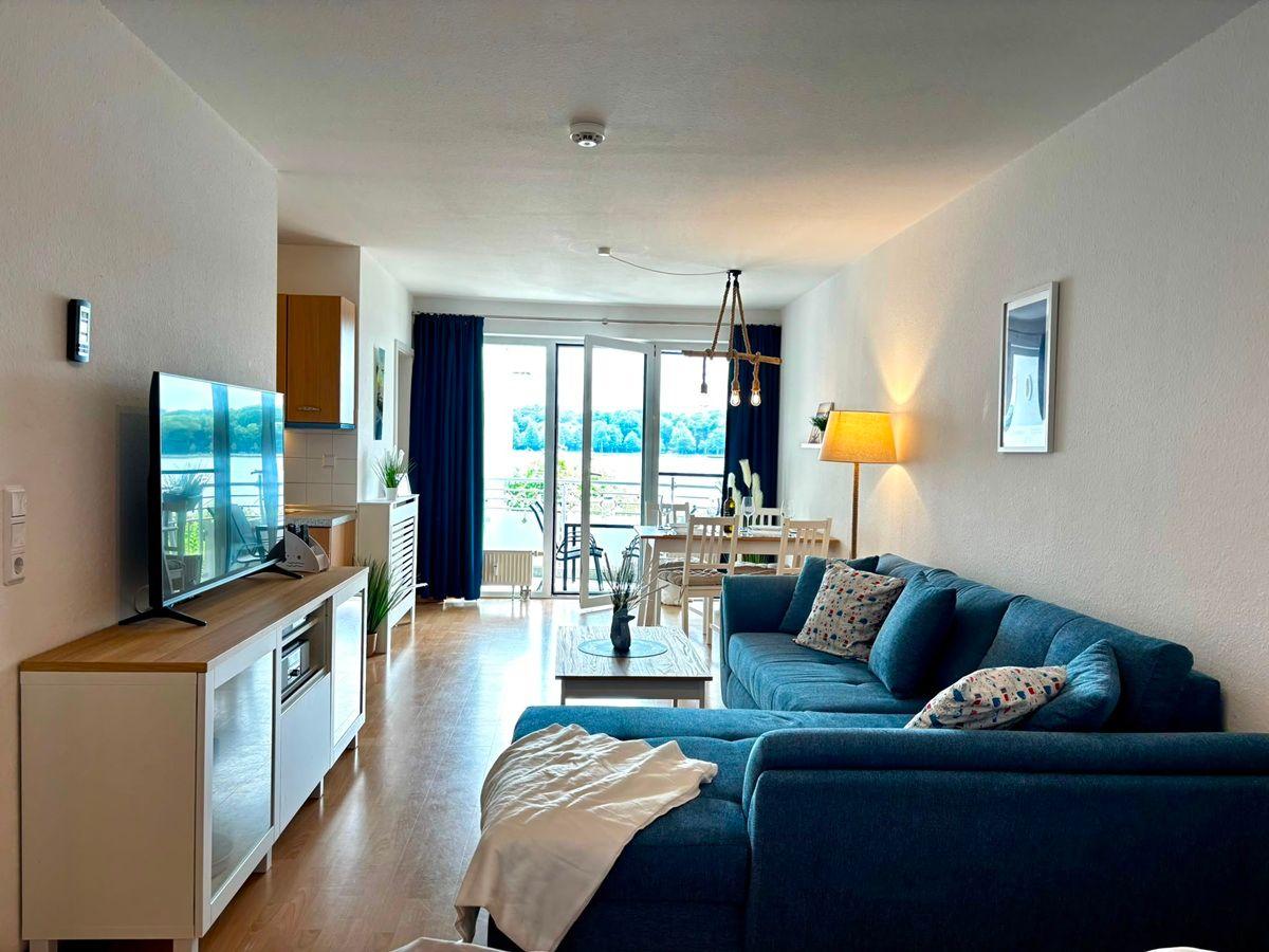Wohnzimmer mit Sofa, Fernseher und Blick auf den See.