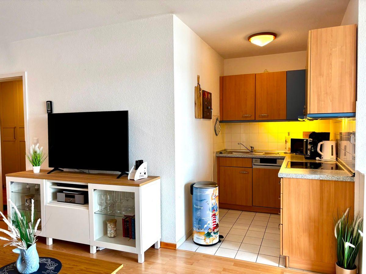 Wohnbereich mit TV und Küche mit Holzschränken und Arbeitsfläche.