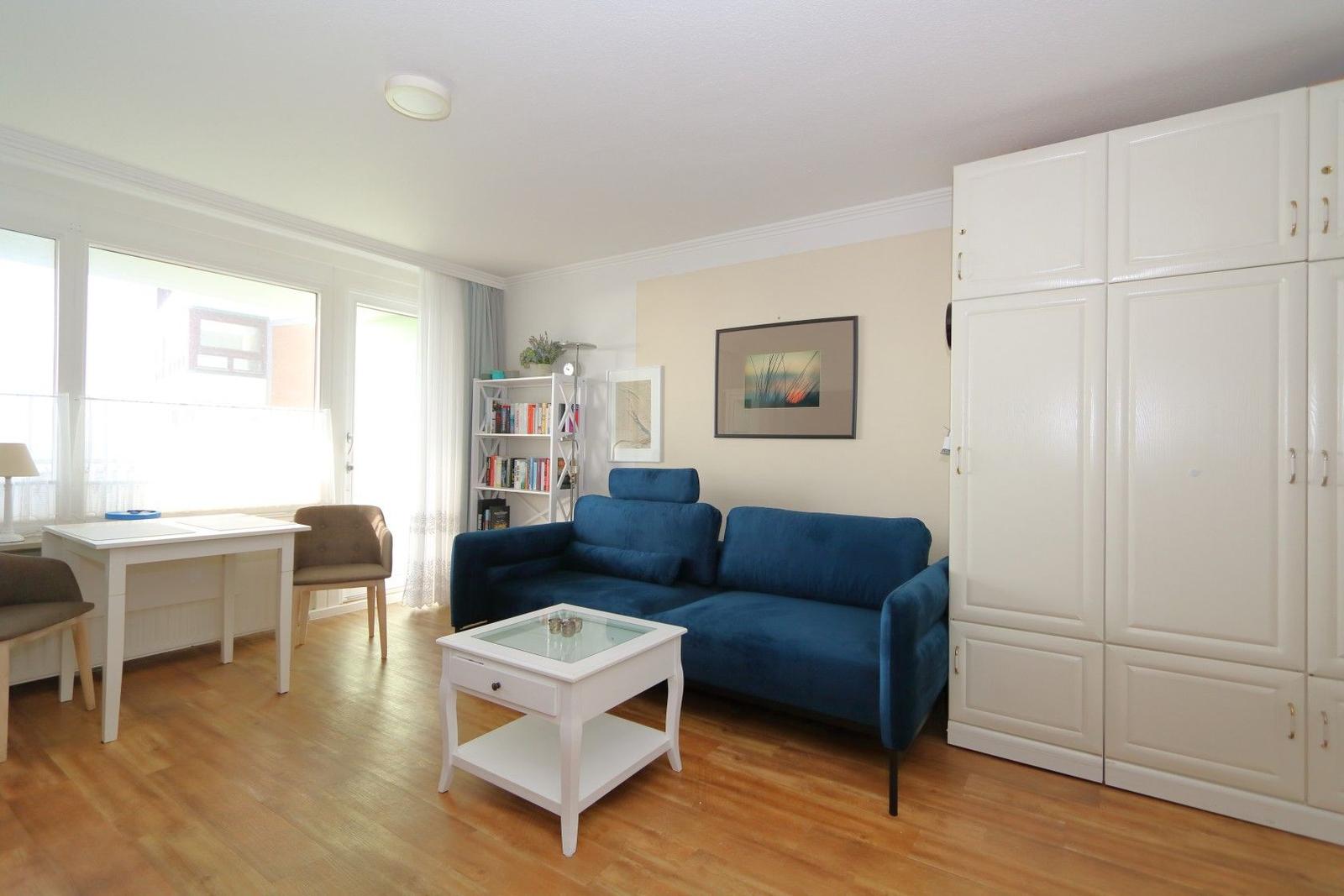 Living room with blue sofa, white furniture, and wooden floor. Windows and curtains visible.