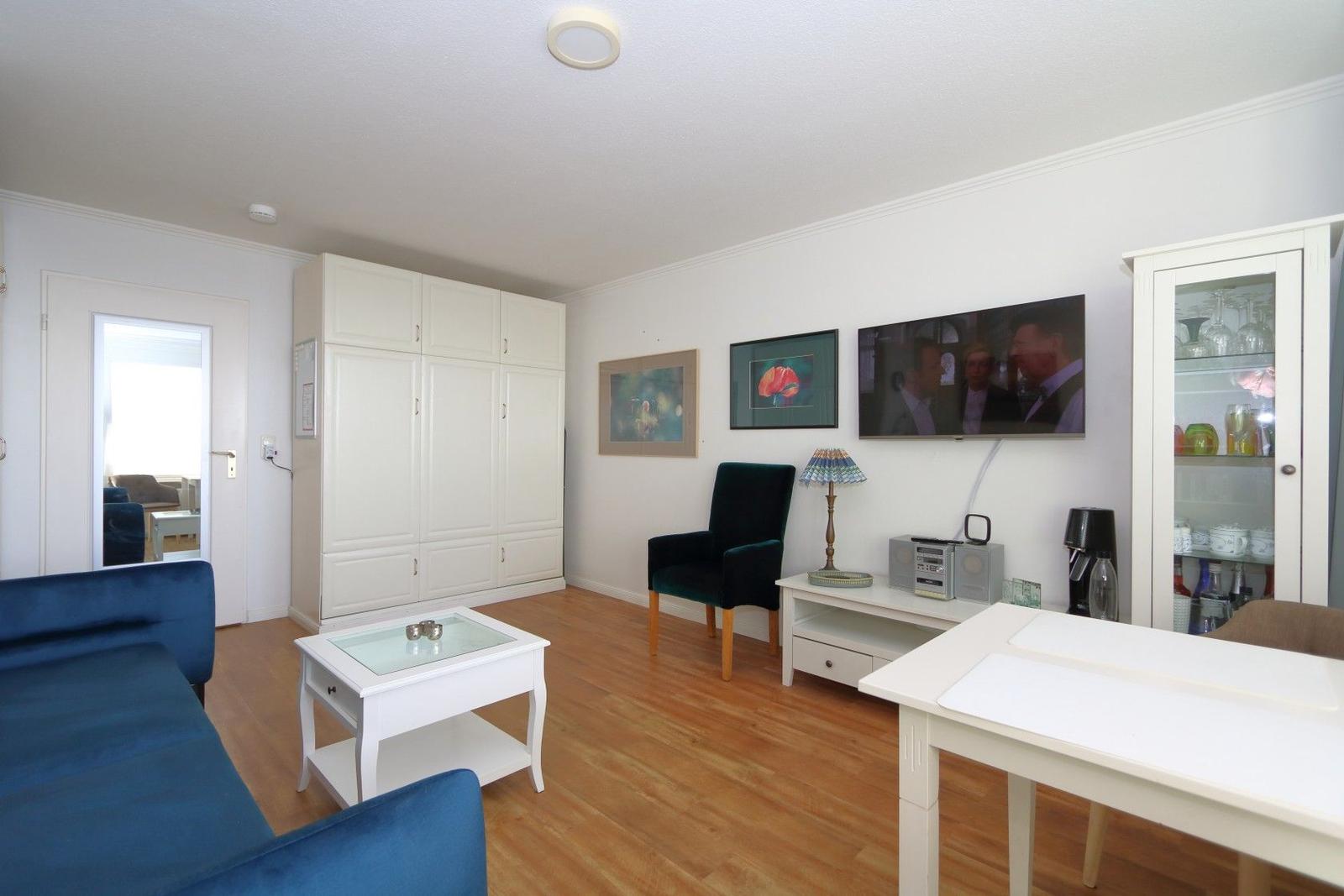 Living room with blue sofa, white table, and TV mounted on the wall.