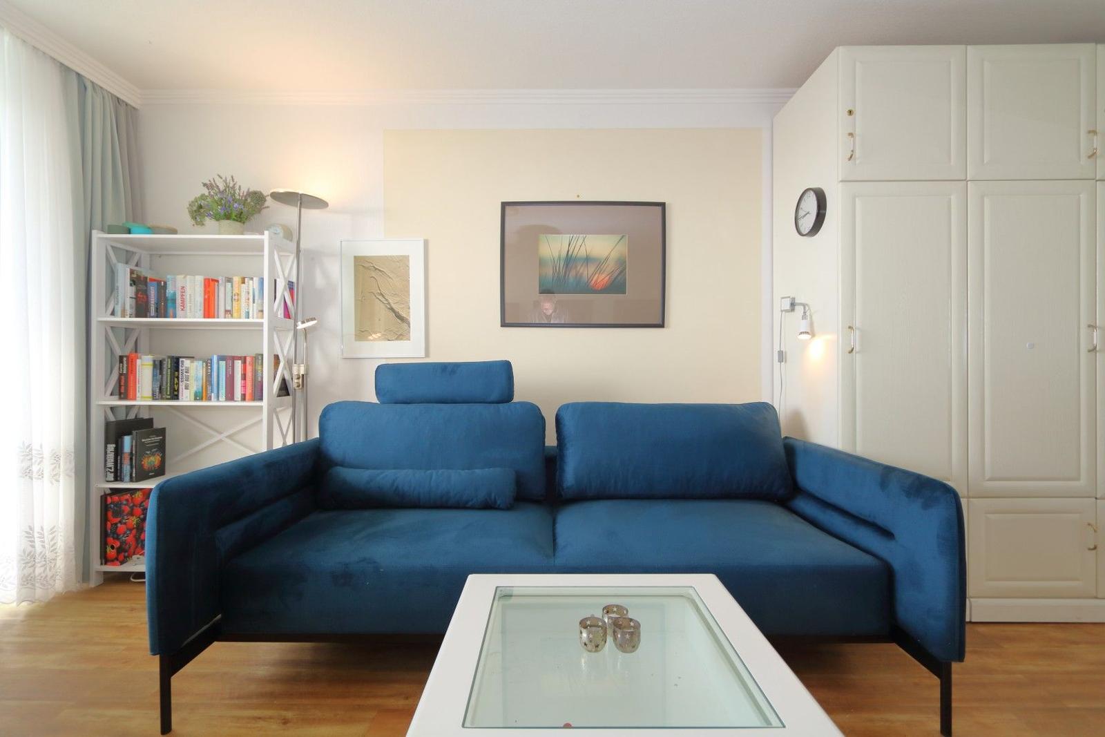 Blue sofa in living room with glass table and white shelves.