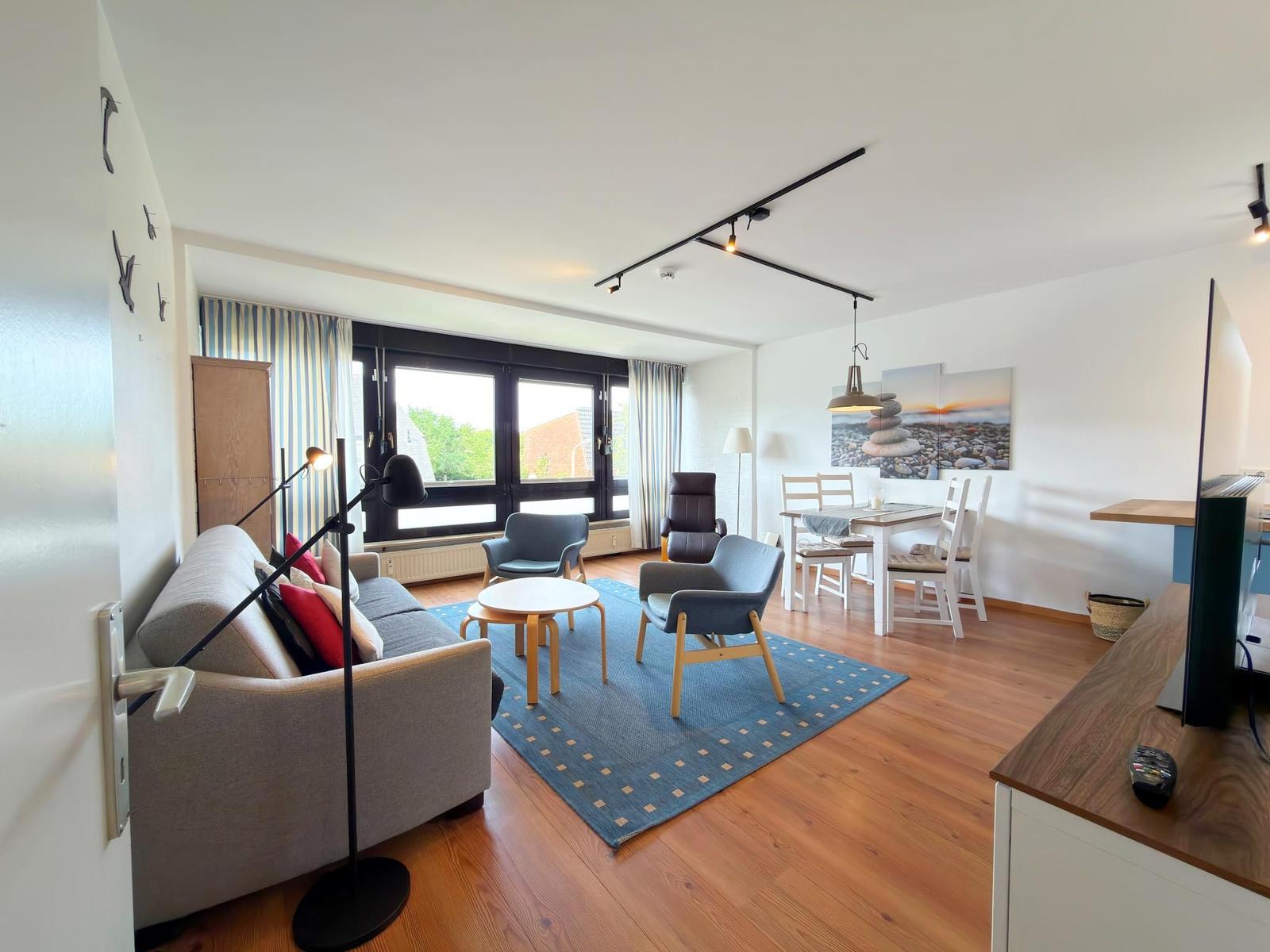 Wohn- und Essbereich mit Sofa, Stühlen und Tisch. Holzboden und große Fenster.