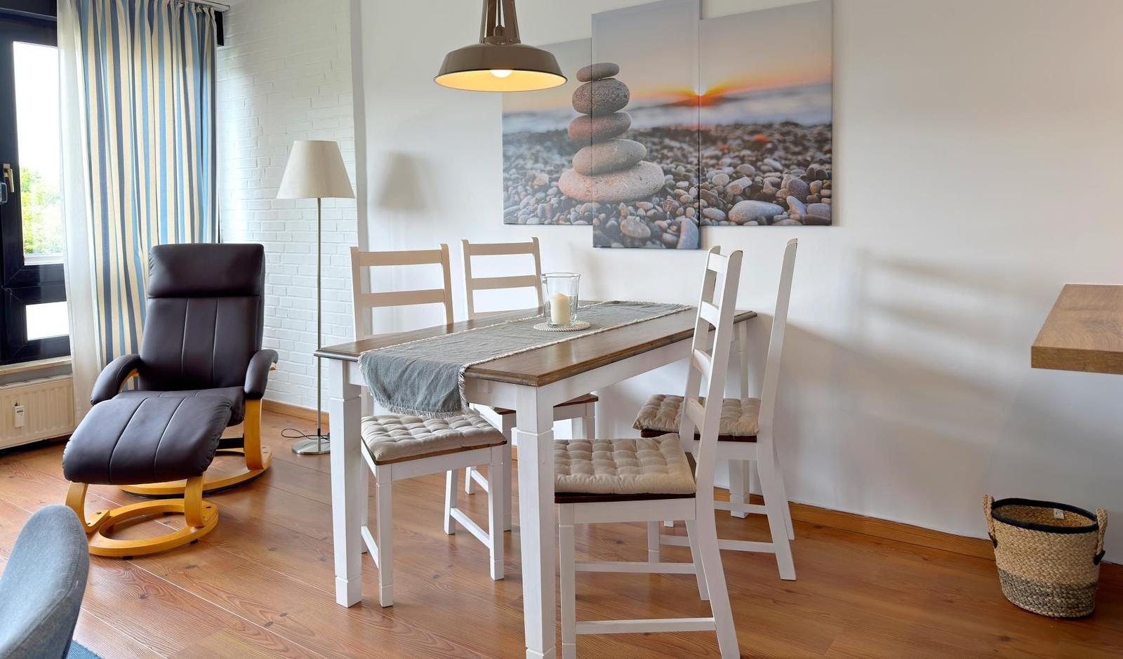 Esszimmer mit Tisch, Stühlen und Wandbild. Holzboden und Fenster mit Vorhängen.
