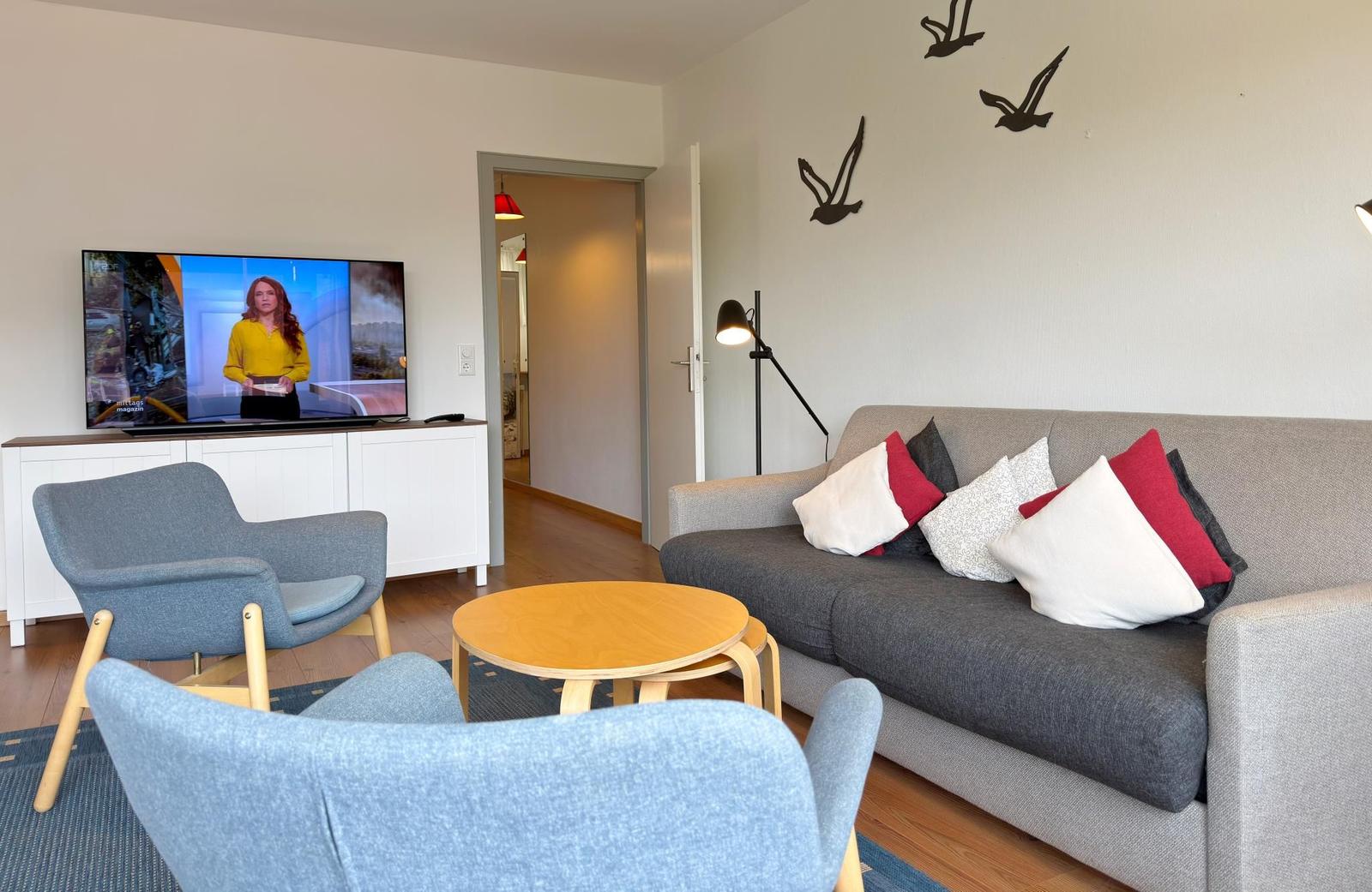 Wohnzimmer mit Sofa, Sessel und Fernseher. Wanddekoration mit Vogelmotiven.