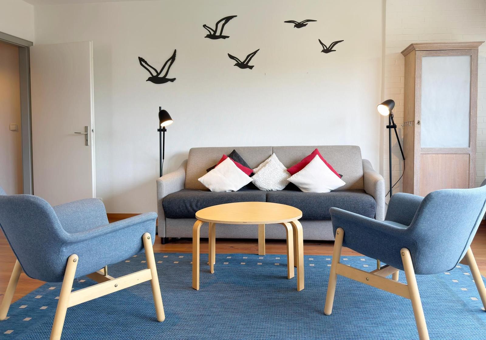 Wohnzimmer mit Sofa, zwei Stühlen, Tisch und Wanddekoration.