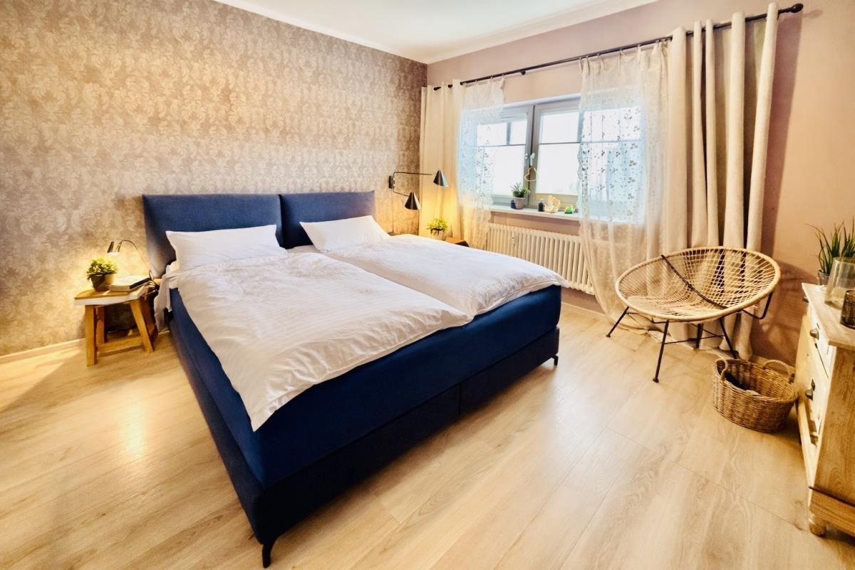Schlafzimmer mit Doppelbett, Fenster, Stuhl und Holzboden.