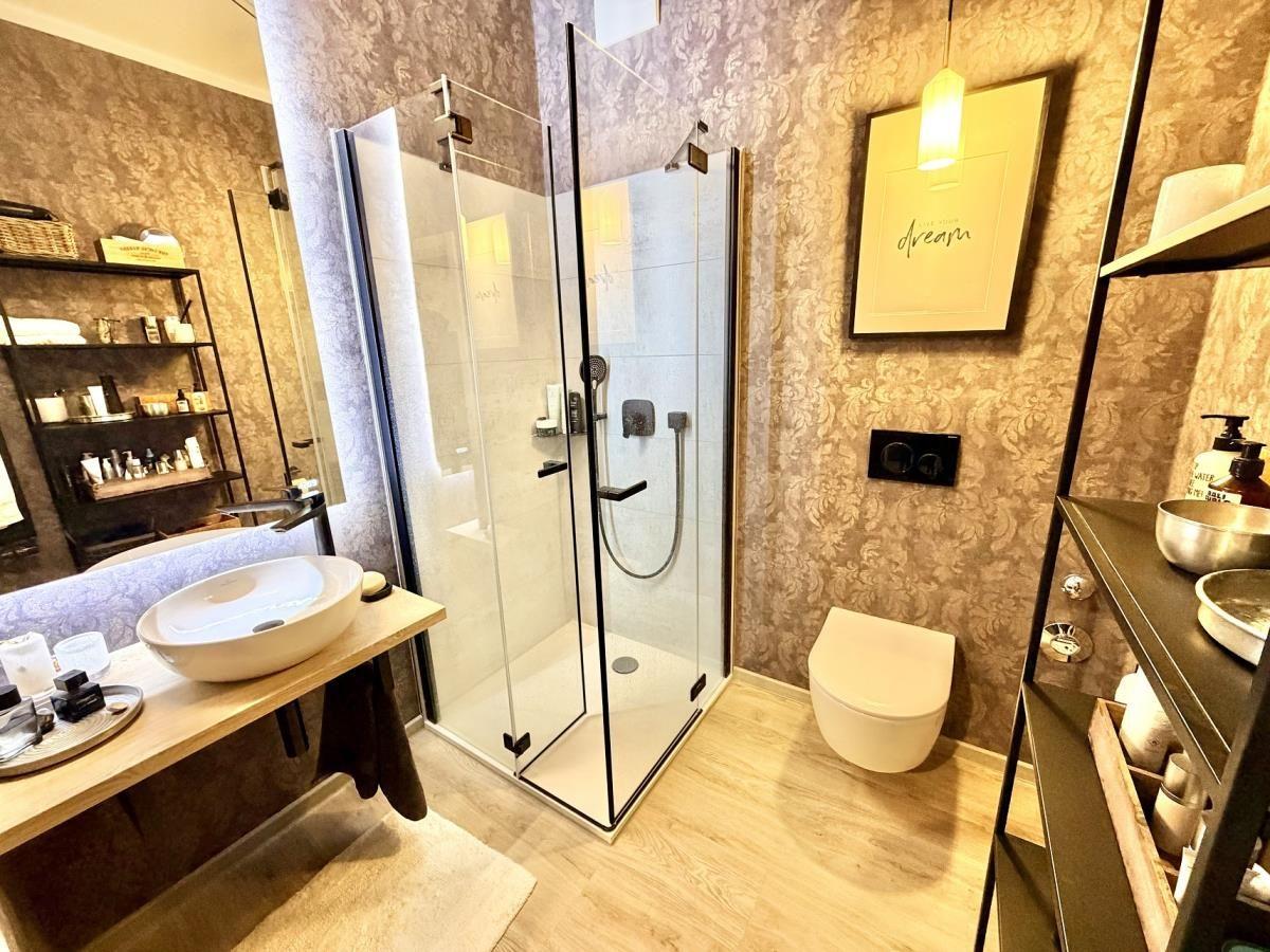 Bad mit Dusche, Waschbecken und Toilette. Tapete, Holzboden und Regale.