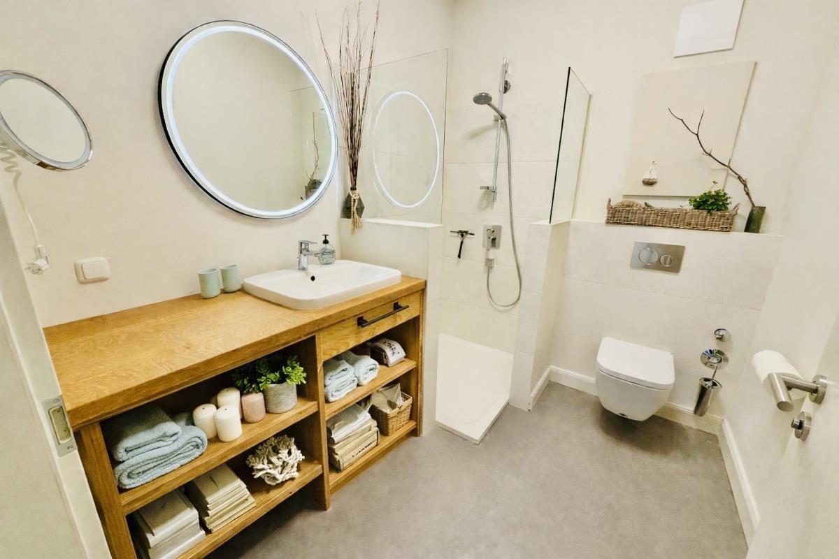 Badezimmer mit Waschbecken, Dusche und Toilette. Holzregal mit Handtüchern und Dekoration.