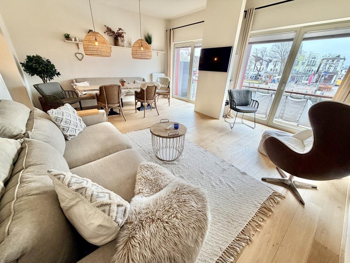Wohnzimmer mit Sofa, Tisch und Sessel. Große Fenster mit Blick auf den Hafen.