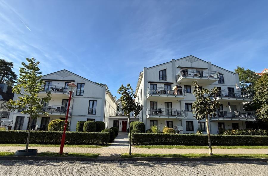 Zwei weiße Mehrfamilienhäuser mit Balkonen und begrünten Flächen unter blauem Himmel.