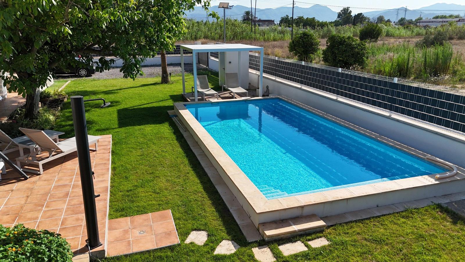 Pool mit Sonnenschutz, Liegen und Grünfläche. Berglandschaft im Hintergrund.