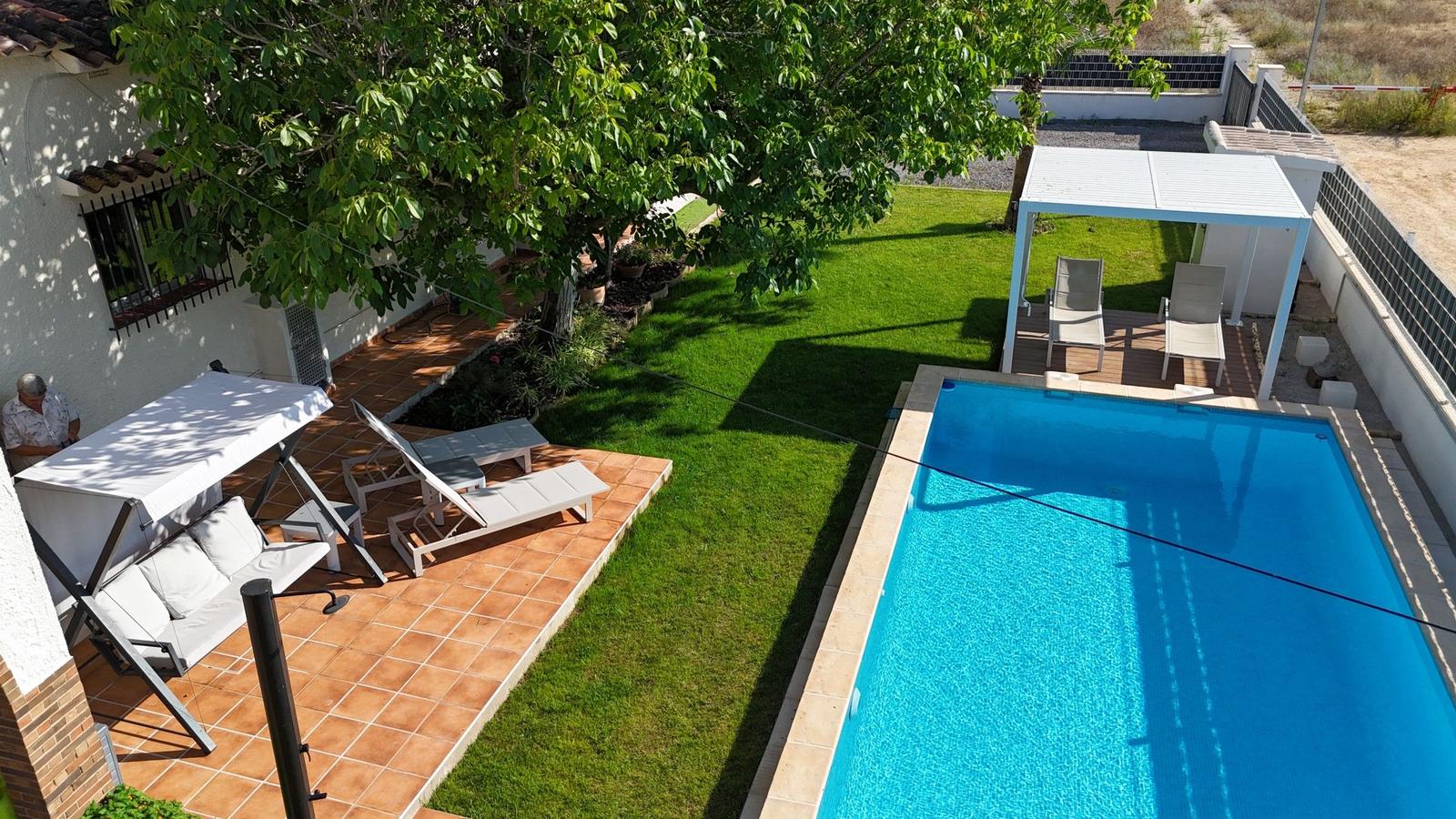 Pool mit Liegestühlen und Terrasse unter Bäumen im Garten