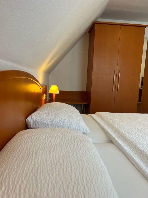 Doppelbett mit weißer Bettwäsche, Nachttisch mit Lampe und Schrank unter schräger Decke.