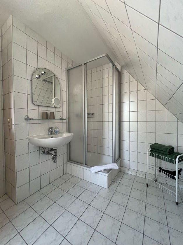 Badezimmer mit Dusche, Waschbecken und Spiegel an geneigter Decke.