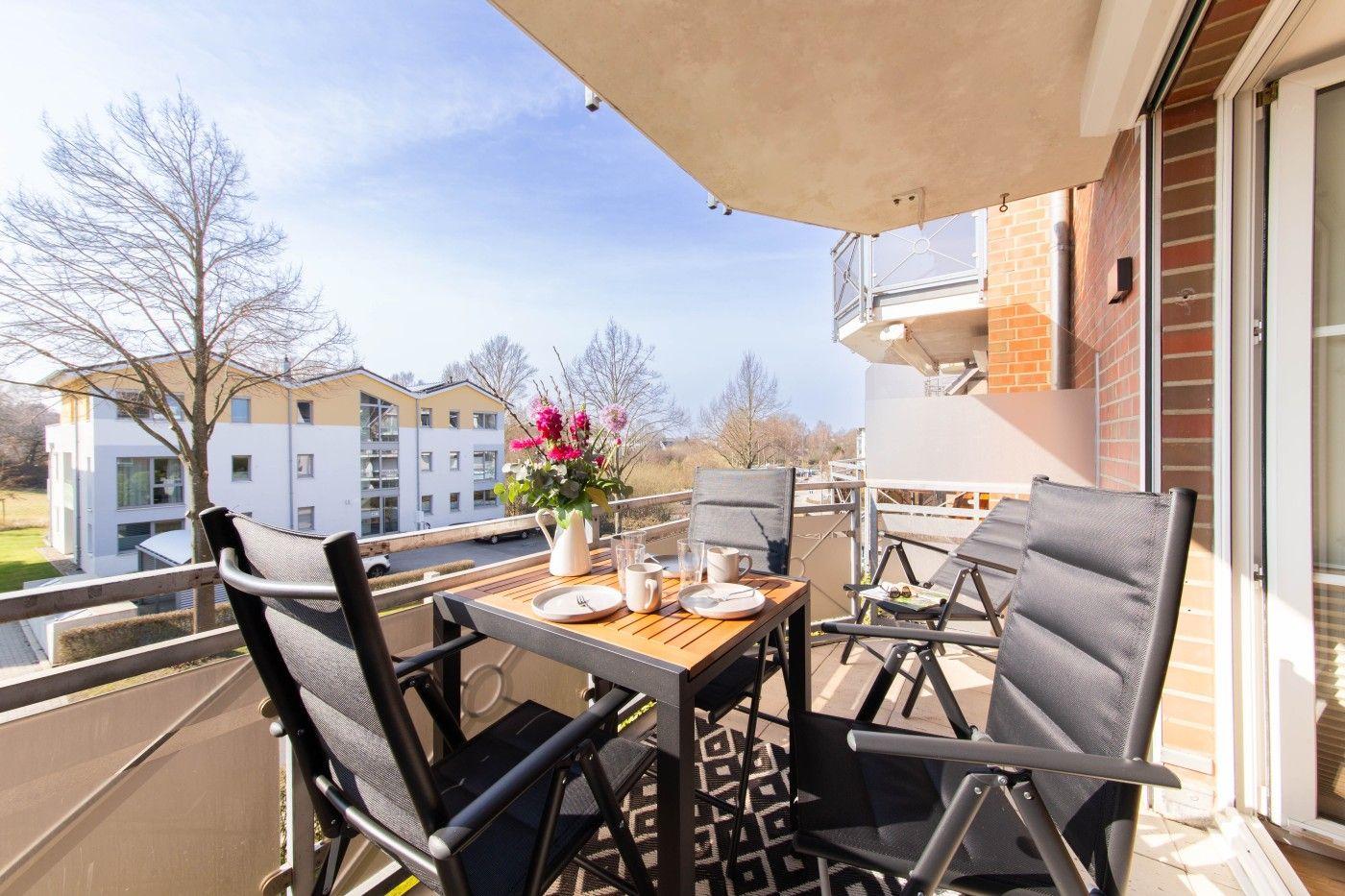 Terrasse mit Tisch, Stühlen und Blumen. Blick auf Wohnhäuser und Bäume.