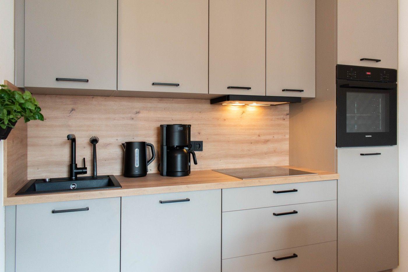 Küche mit Holzrückwand, schwarzen Armaturen und integriertem Backofen.