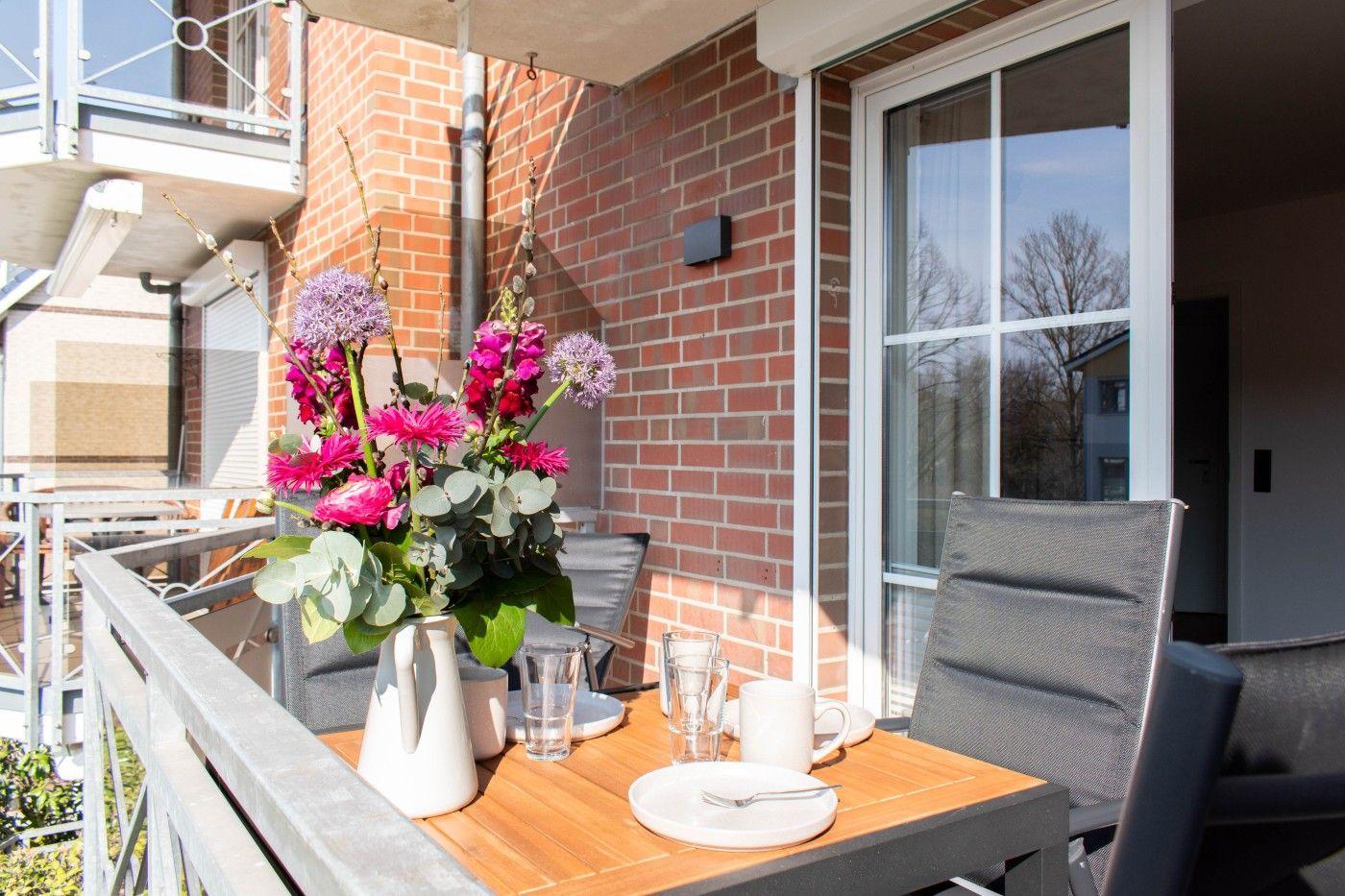 Terrasse mit Tisch, Stühlen und Blumenarrangement vor Backsteinmauer und Fenster.