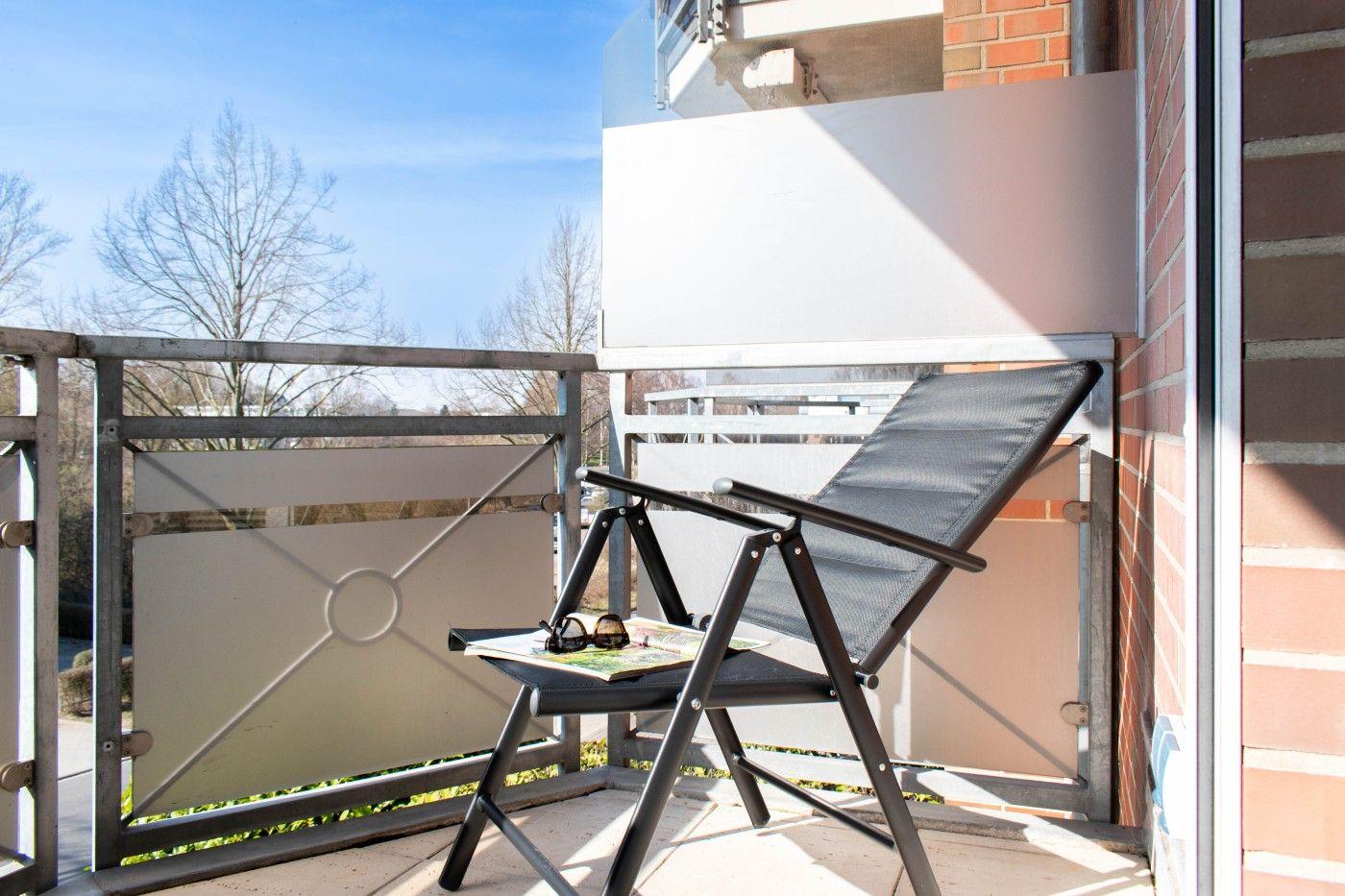 Terrasse mit Liegestuhl, Sonnenschutz und Blick auf Bäume.