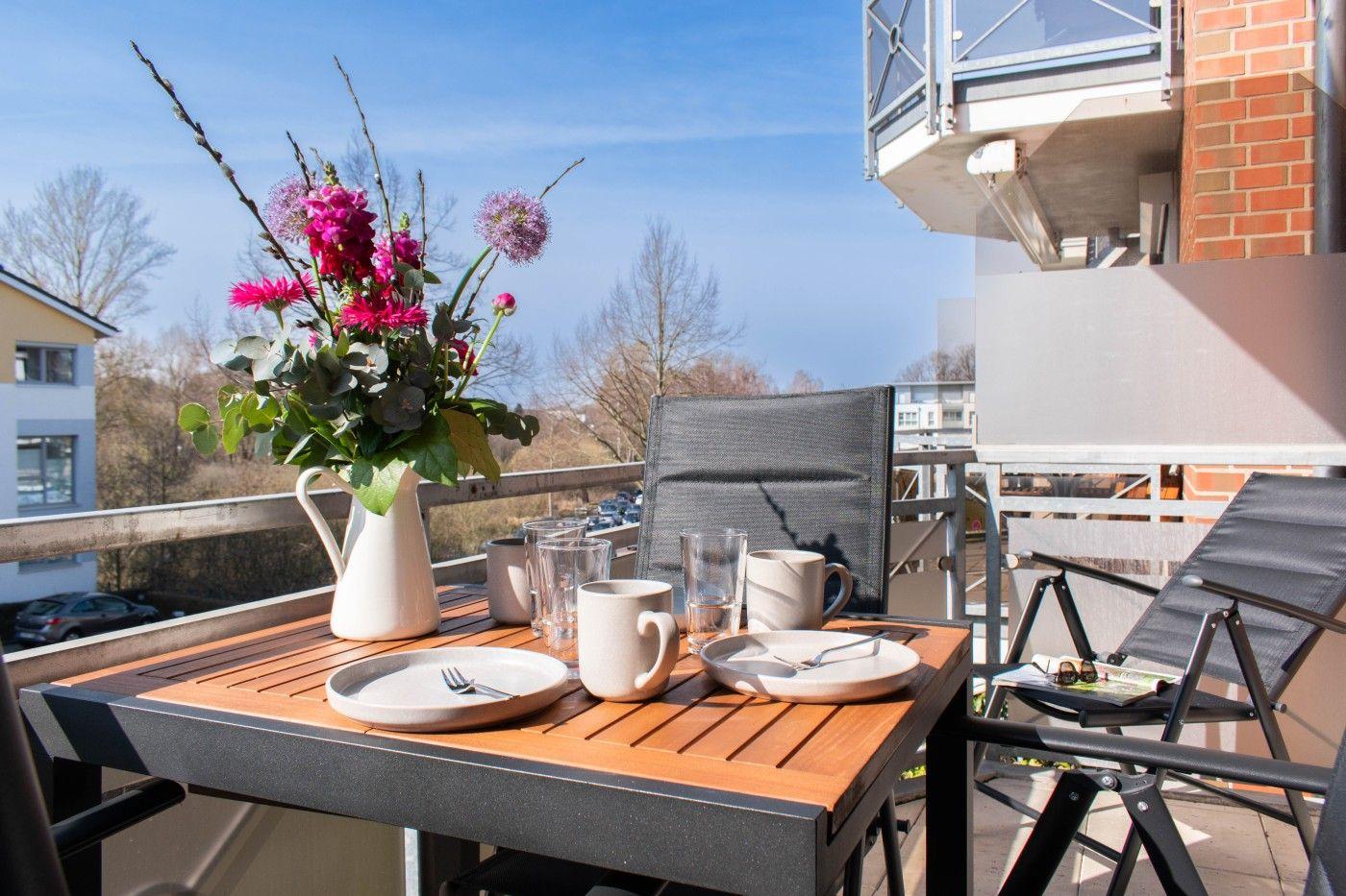 Terrasse mit Tisch, Stühlen und Blumenarrangement. Blick auf Wohngebiet und Himmel.