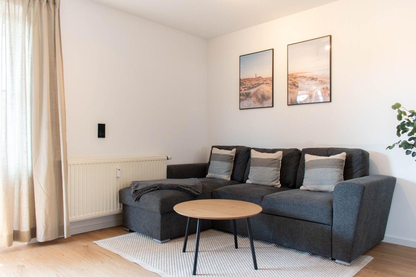 Ein Wohnzimmer mit grauem Sofa, runder Tisch und zwei Wandbildern.