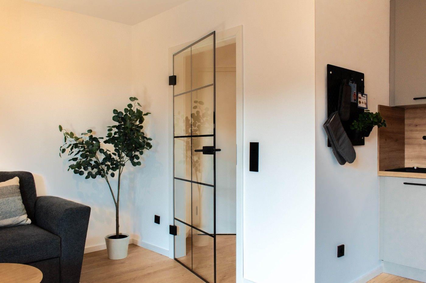 Wohnbereich mit Glaswand, Pflanze und Sofa. Küchenbereich mit Holzoberfläche.