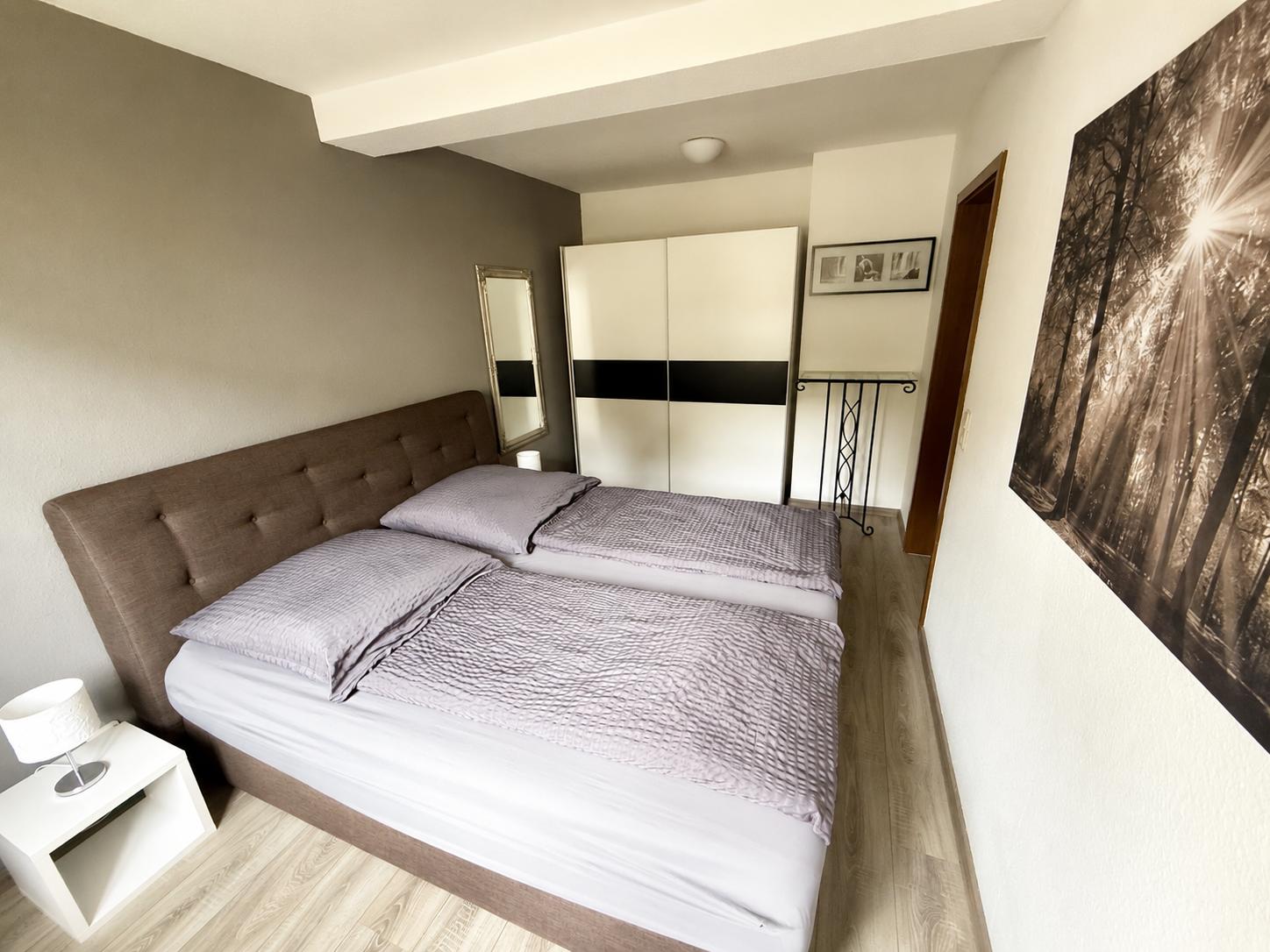 Schlafzimmer mit Doppelbett, Kleiderschrank und Wandbild.
