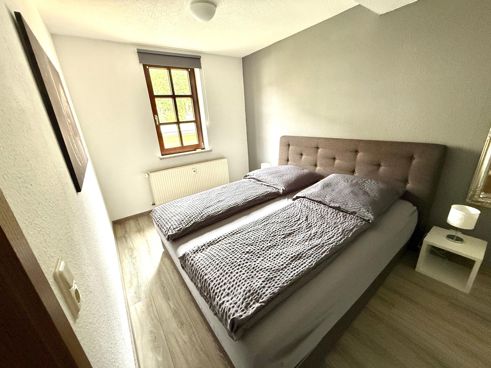 Schlafzimmer mit Doppelbett, Fenster und Nachttisch.