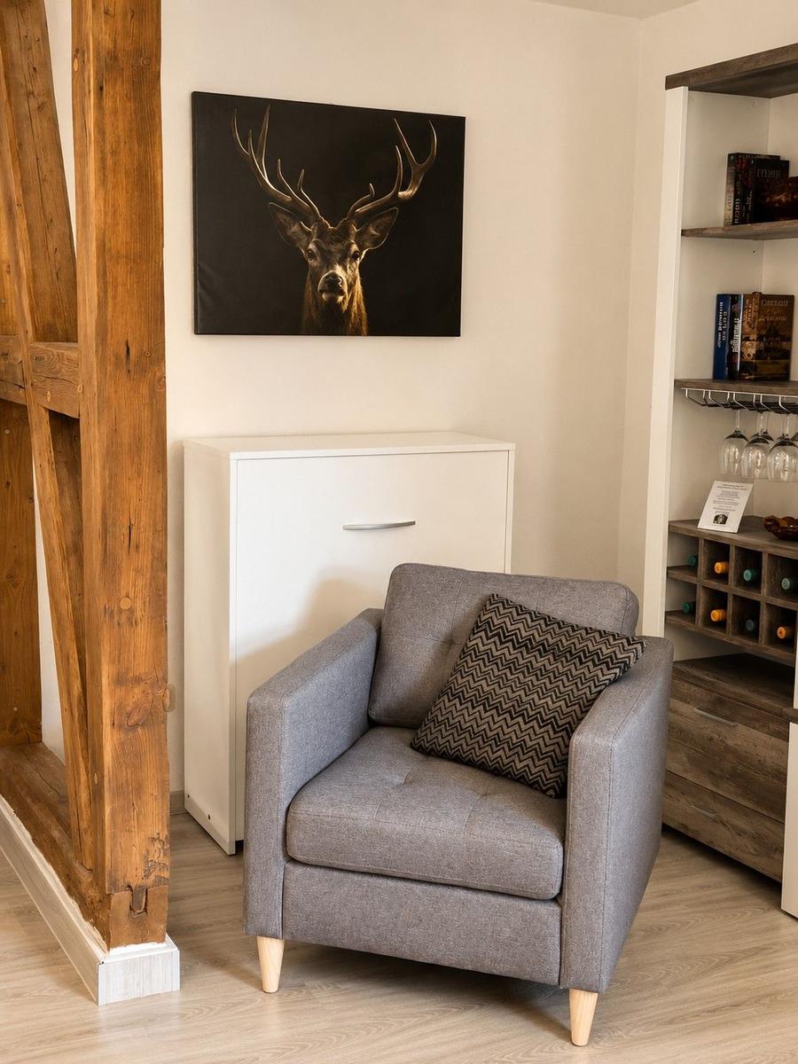 Ein grauer Sessel mit Kissen steht vor einer Wand mit Bild und Schrank.