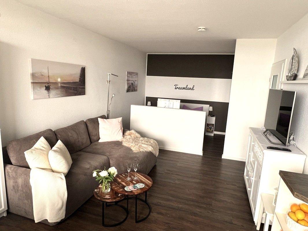 Living area with sofa, coffee table, and TV. Background: sleeping area with bed.