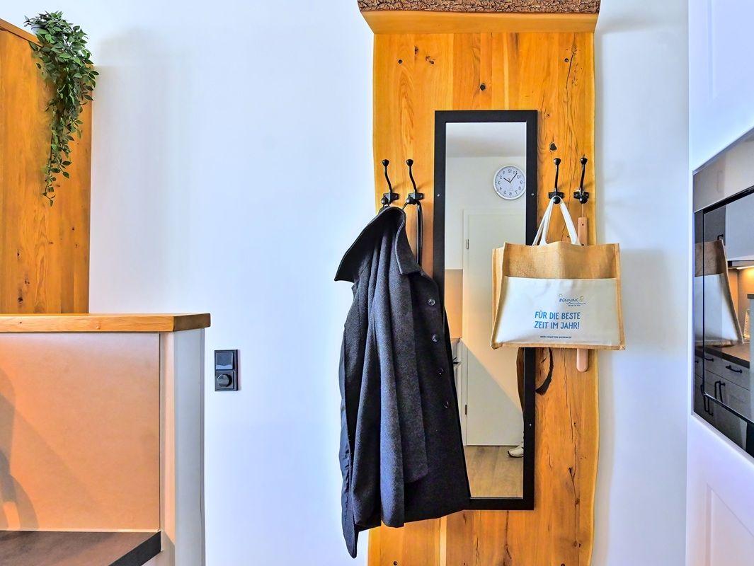 Haus-Eingang mit Holzwand, Spiegel und Haken für Jacke und Tasche.