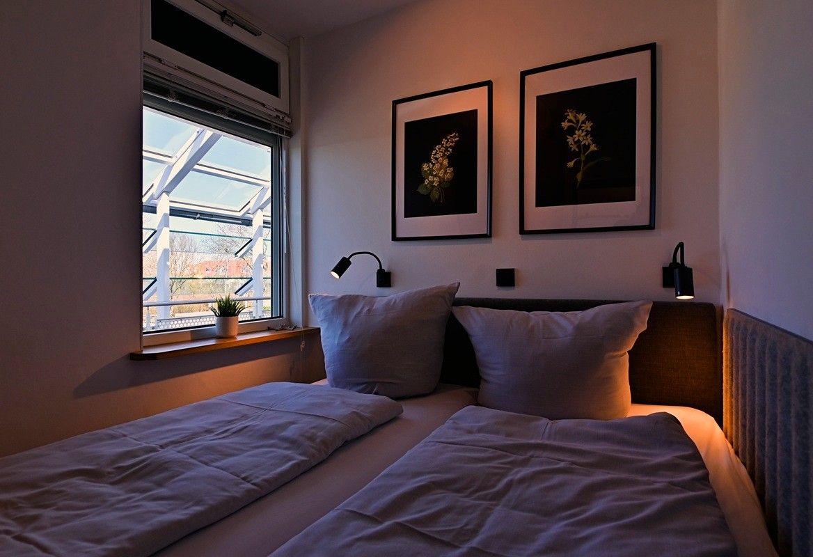 Schlafzimmer mit Doppelbett, Fenster und zwei Wandbildern mit Blumenmotiven.