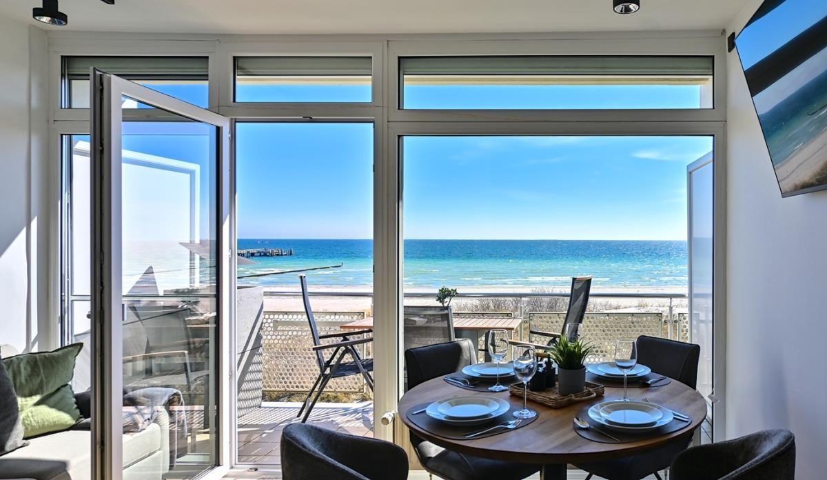 Dinner-Tisch mit Meerblick durch große Fenster. Terrasse mit Stühlen und Blick auf das Meer.