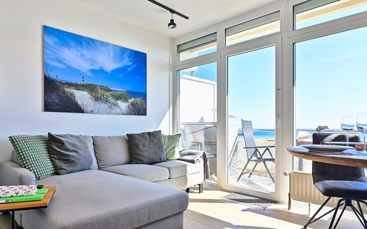 Wohnbereich mit Sofa, Tisch und Blick auf Balkon mit Meerblick.
