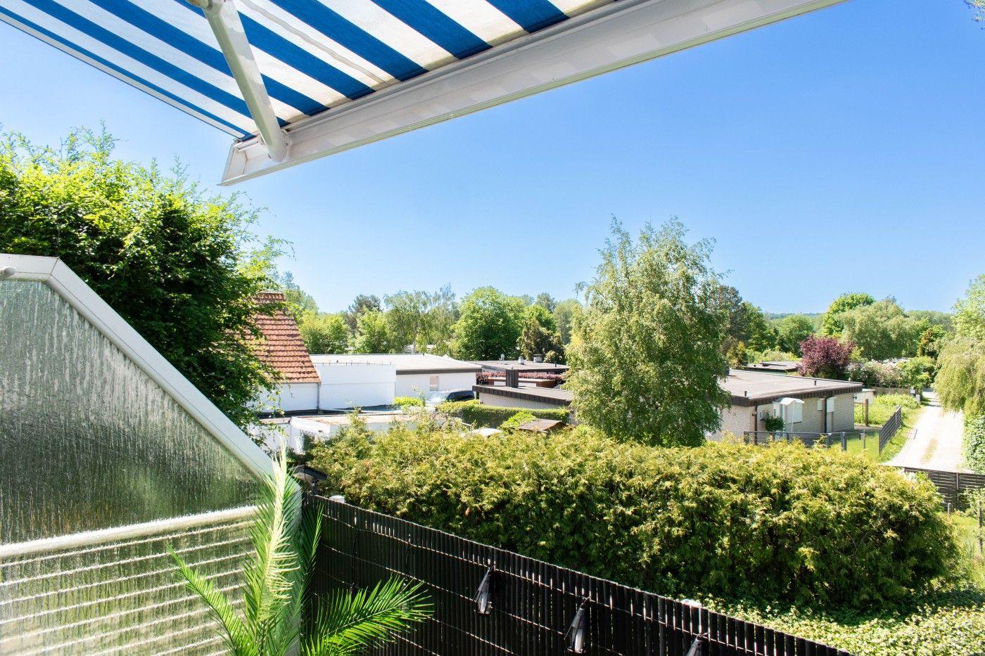 Terrasse mit blau-weißem Markisenüberdachung, Blick auf grüne Bäume und Häuser im Hintergrund.