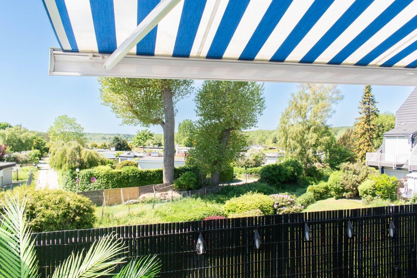 Terrasse mit blau-weißem Markisenüberdachung, Blick auf grüne Gärten und Bäume.