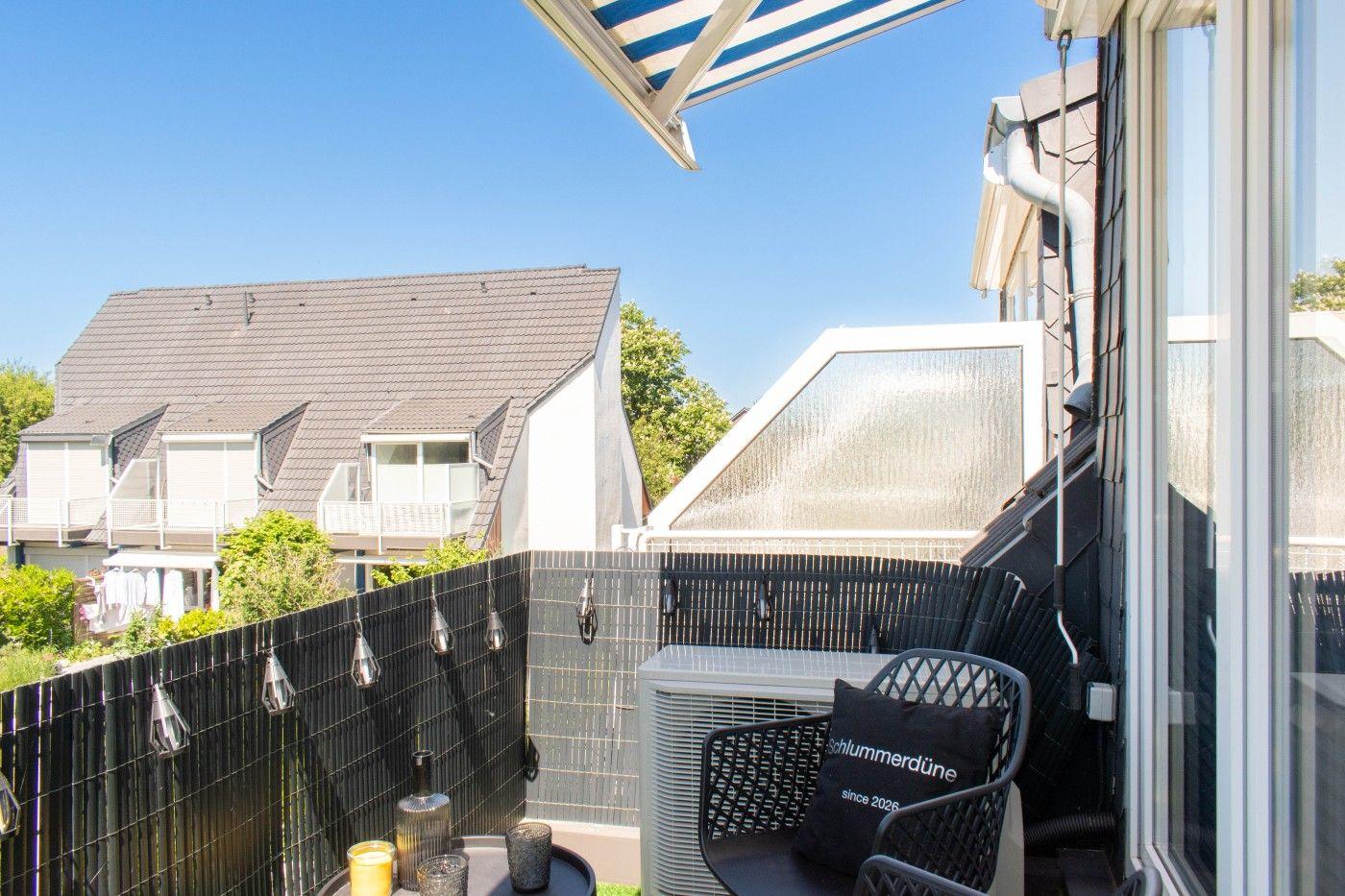 Terrasse mit Sitzgelegenheit und Sonnenschutz, Blick auf Nachbarhäuser und grüne Umgebung.