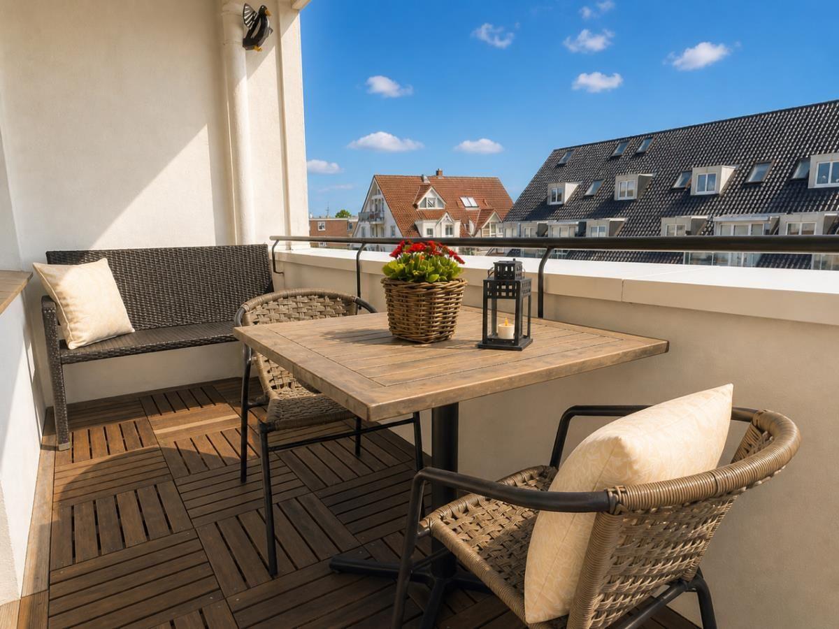 Terrasse mit Tisch, zwei Stühlen und Sitzbank. Blick auf Dächer und blauen Himmel.