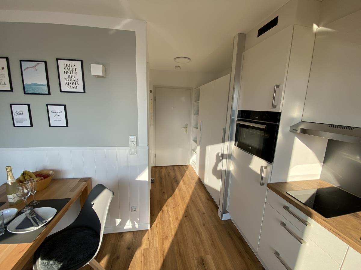 Küche mit Essbereich, weiße Schränke und Holzboden. Wand mit Bildern.