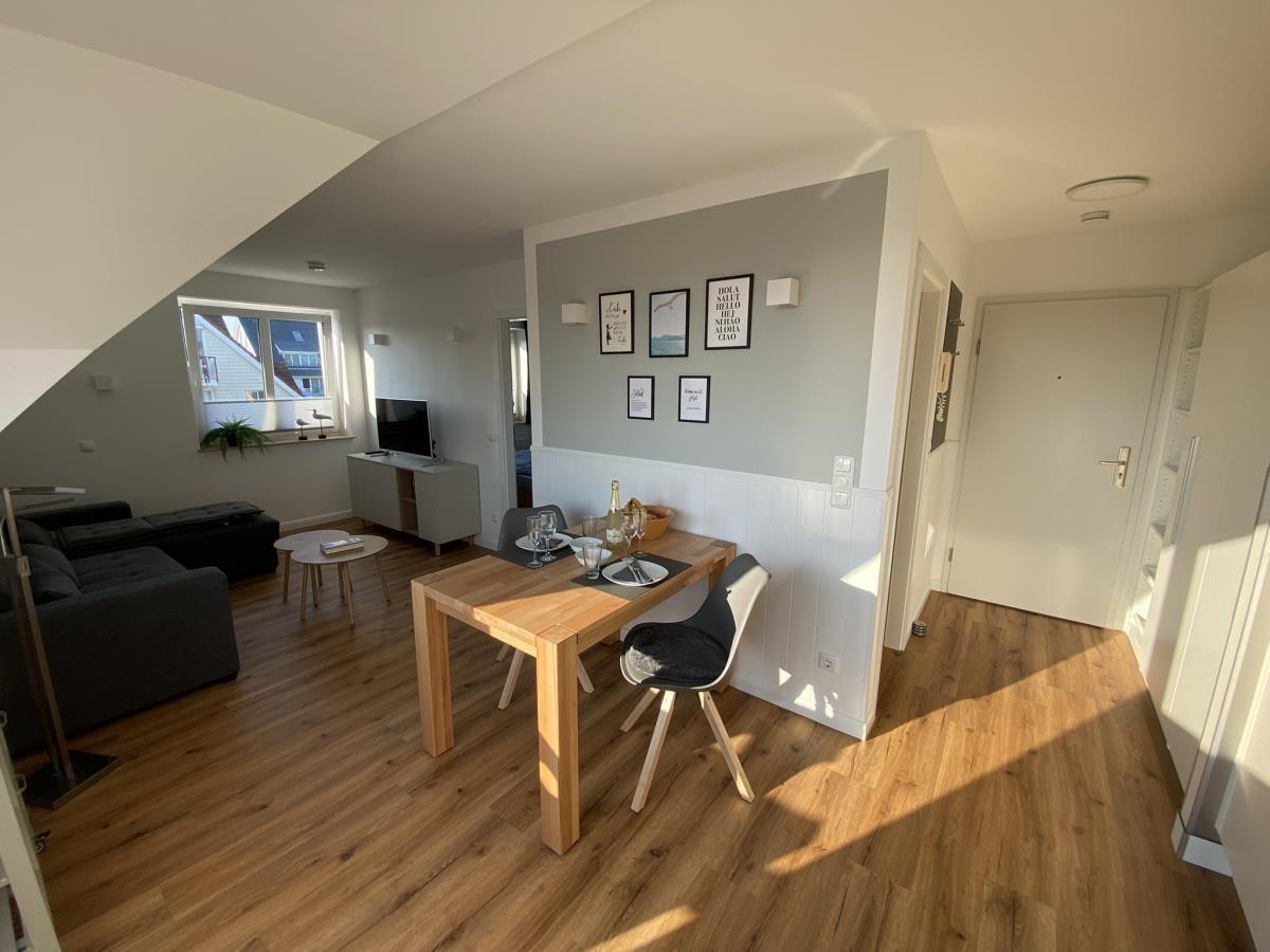 Wohn- und Essbereich mit Holzboden, Esstisch und Sofa. Wand mit Bildern und Fenster.