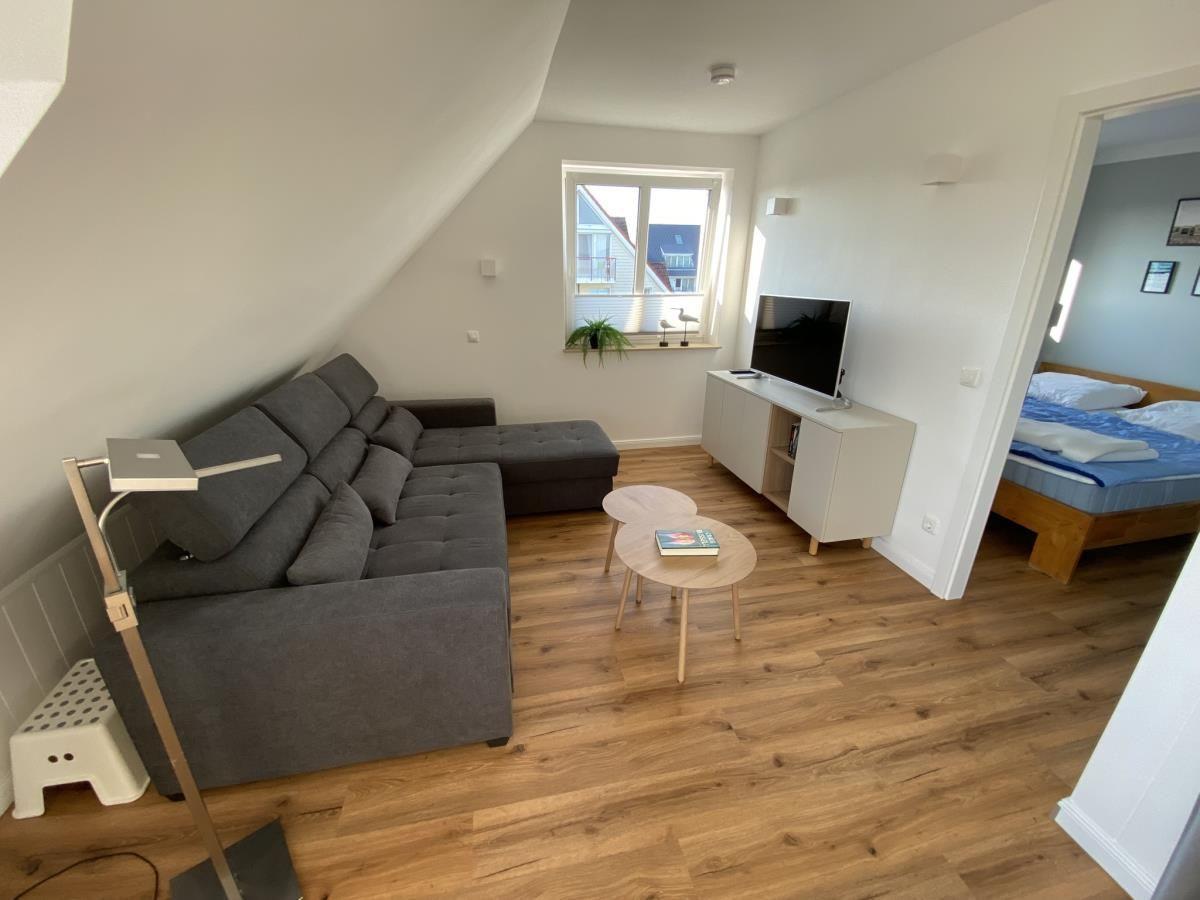 Wohnzimmer mit Sofa, Fernseher und Holzboden. Schlafzimmer mit Bett sichtbar.