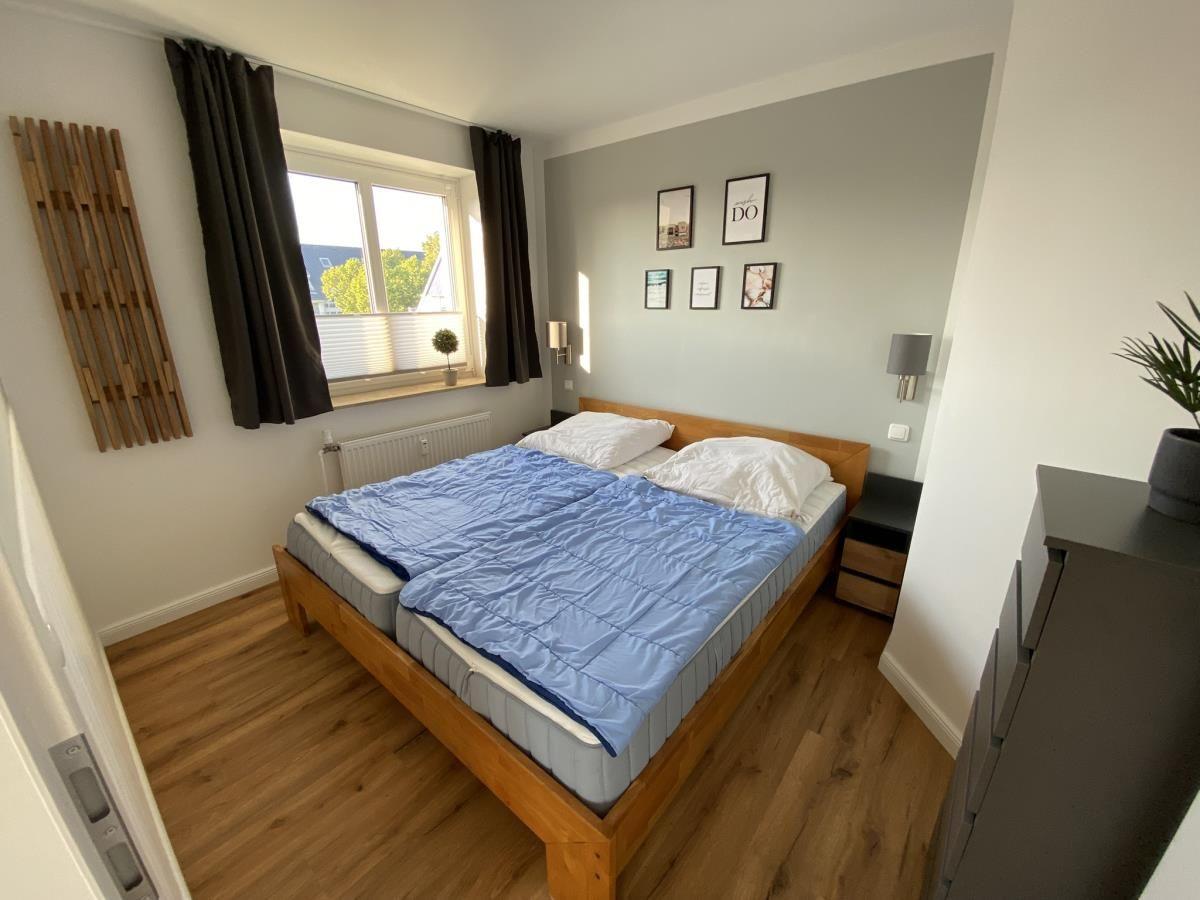 Schlafzimmer mit Holzbett, blauer Bettdecke und Fenster mit Blick.