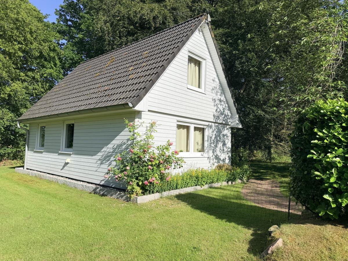 Ein weißes Haus mit dunklem Dach steht im Grünen. Vor dem Haus befindet sich ein Rasen und Blumen.
