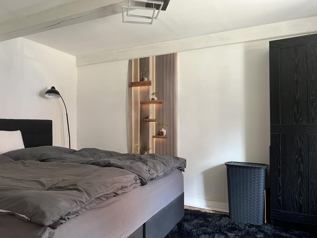 Schlafzimmer mit Bett, Kleiderschrank und dekorativer Wandverkleidung.