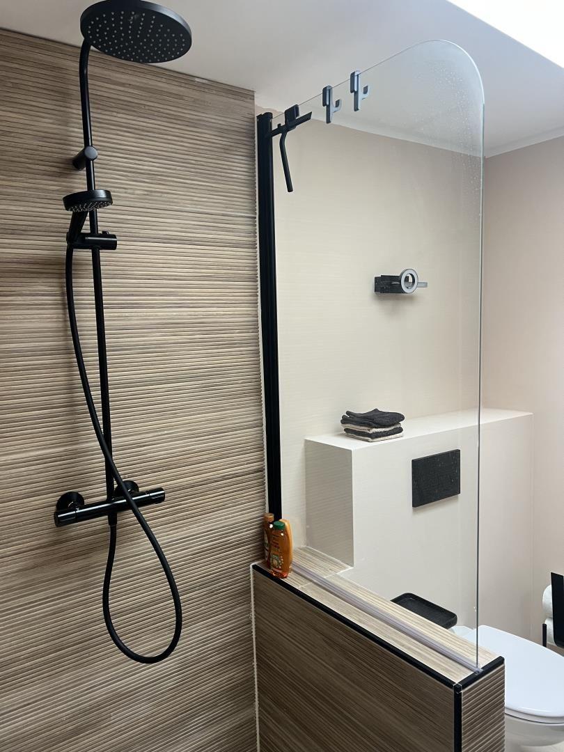 Dusche mit Duschbrause und Glaswand. Toilette und Handtuchständer sichtbar.