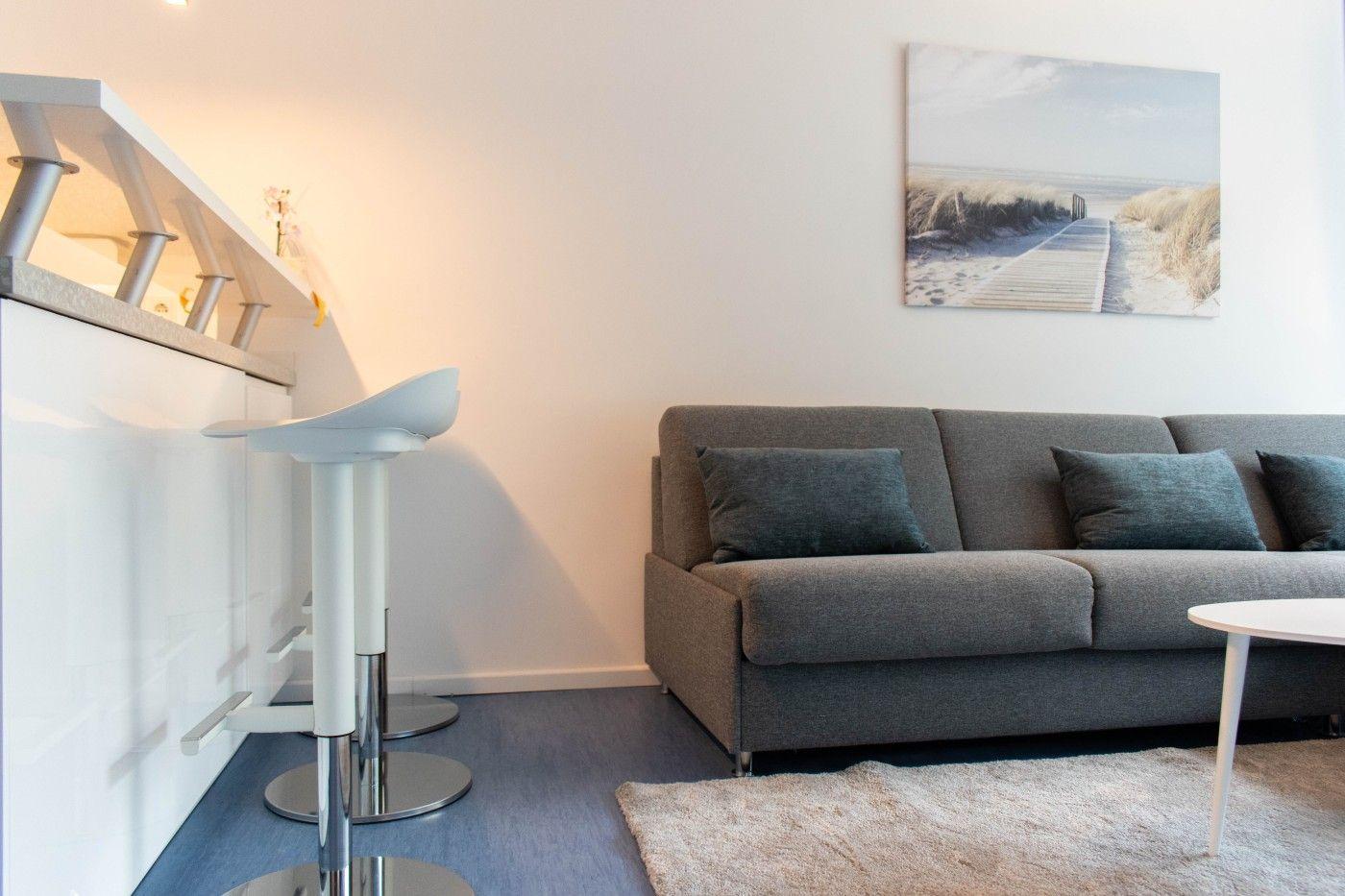 Ein Wohnbereich mit grauem Sofa, Barhocker und Wandbild.