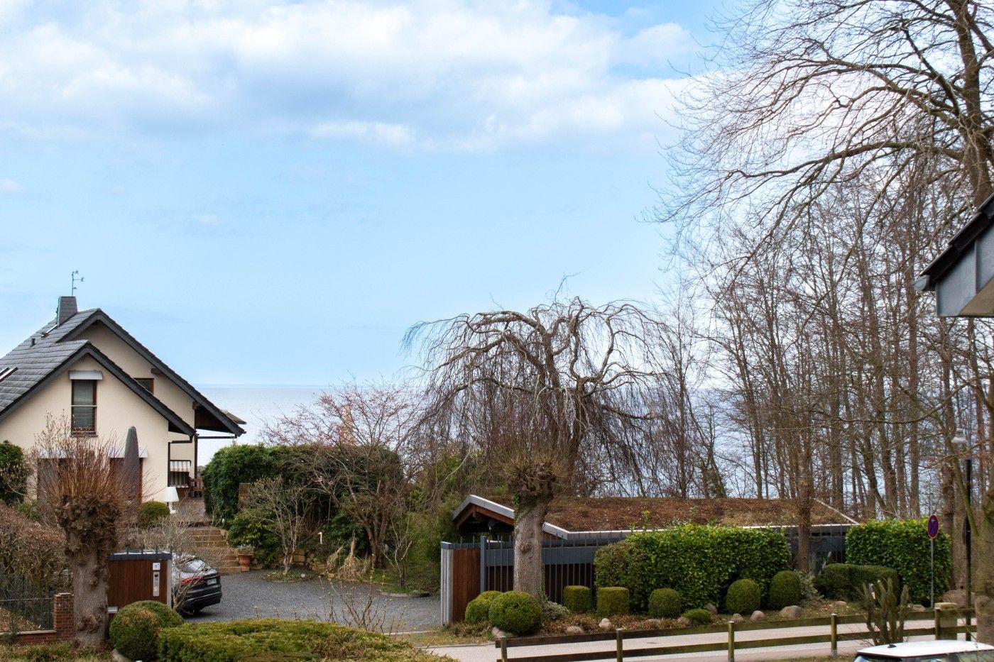 Haus mit Garten, Zaun und Bäumen unter blauem Himmel.