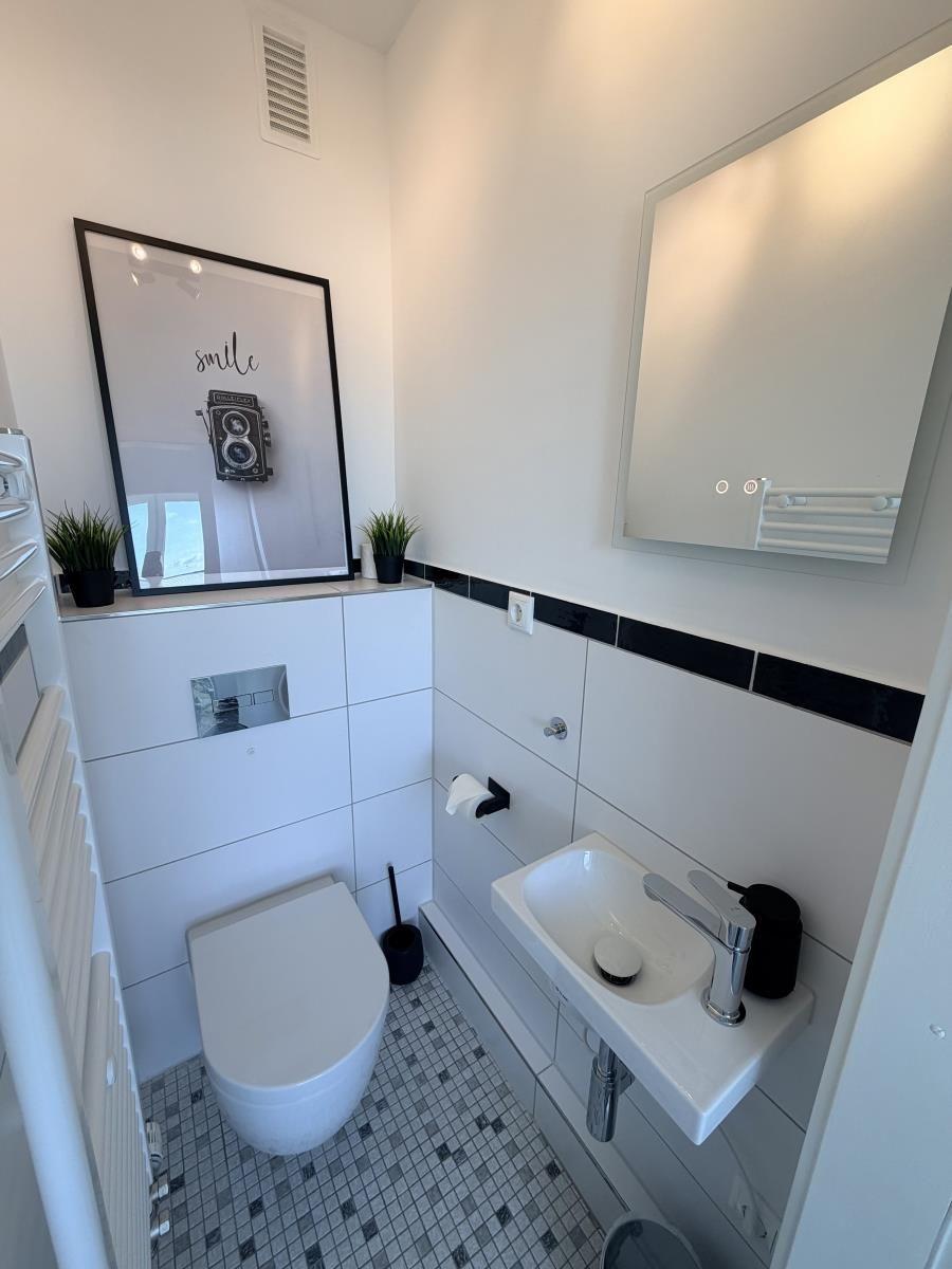 Badezimmer mit Toilette, Waschbecken und Spiegel. Wand mit schwarzem Streifen und Mosaikboden.