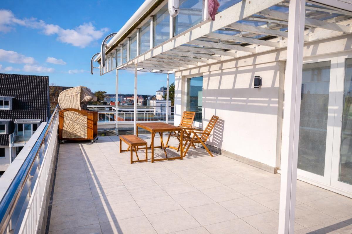 Terrasse mit Tisch, Stühlen und Liegestuhl. Blick auf Stadt und Himmel.