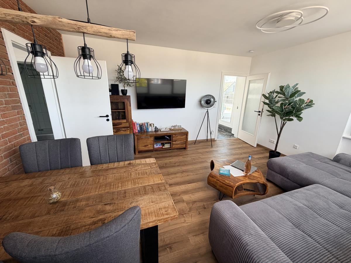 Wohn- und Essbereich mit Holzboden, Sofa, Esstisch und Fernseher.