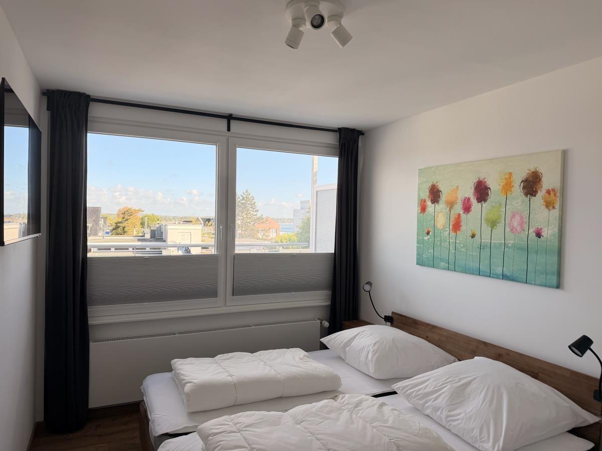 Zimmer mit Doppelbett, Fenster und Wandbild.
